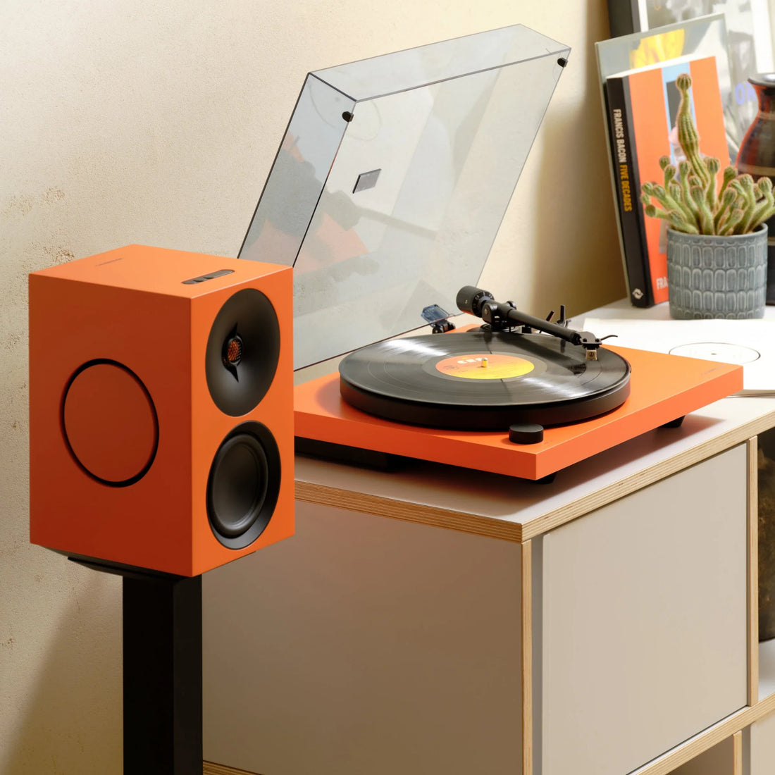 Cambridge Audio Spira turntable in Orange next to an orange L/R speaker on a stand